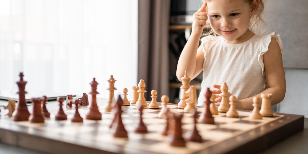 Little girl playing chess at the table in home kitchen. The concept early childhood development and education. Family leisure, communication and recreation. High quality photo